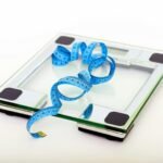 A digital glass weighing scale with a blue measuring tape, symbolizing weight management.