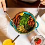A vibrant vegan meal with fresh ingredients like broccoli, chickpeas, quinoa, served alongside a burrito and refreshing drinks.