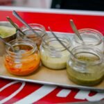 Close-up of colorful sauces in glass jars with spoons on a tray, perfect for culinary presentations.